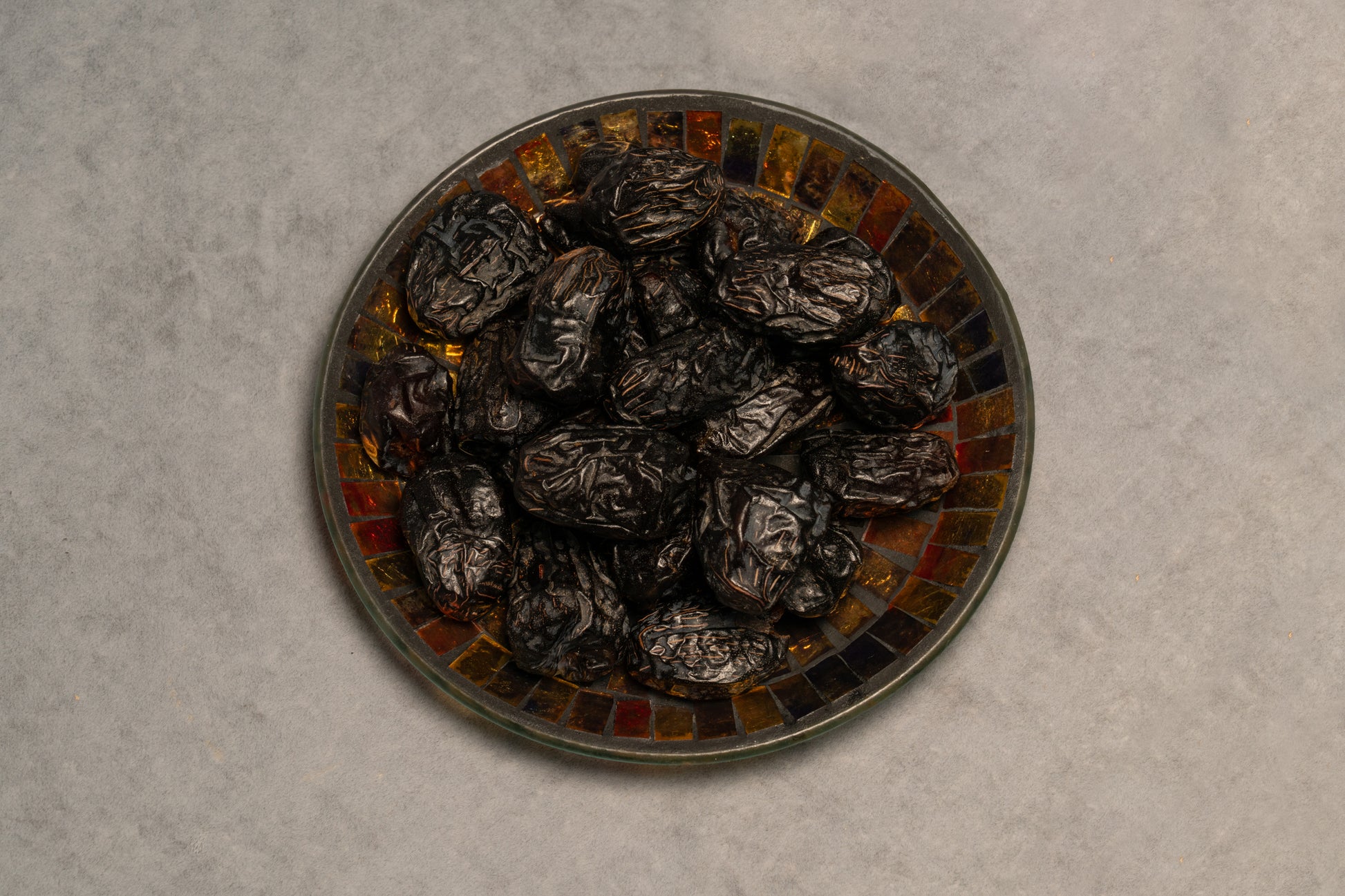 A bowl of Ajwa dates, which are small, dark brown-black in color, and arranged in a pattern that resembles a mosaic tile design.